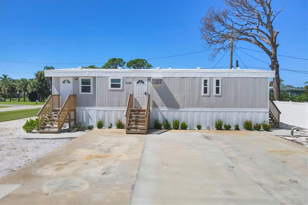 A light gray mobile home with two wooden staircases sits on a concrete driveway — 3280 HOLLY AVENUE, ENGLEWOOD, FL