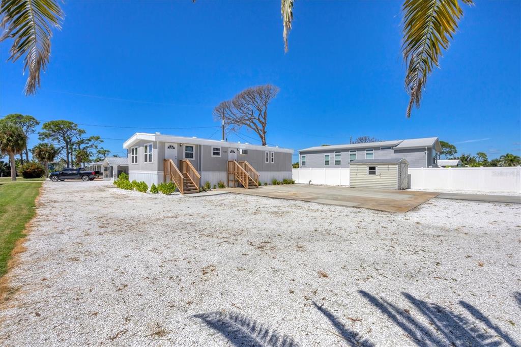 A light gray manufactured home features two wooden staircases and a gravel driveway — 3280 HOLLY AVENUE, ENGLEWOOD, FL