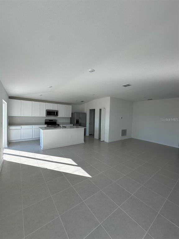 An open-concept kitchen features white cabinetry, a central island, and light-colored tile flooring — 2822 PENNACHIO DRIVE, LAKE WALES, FL