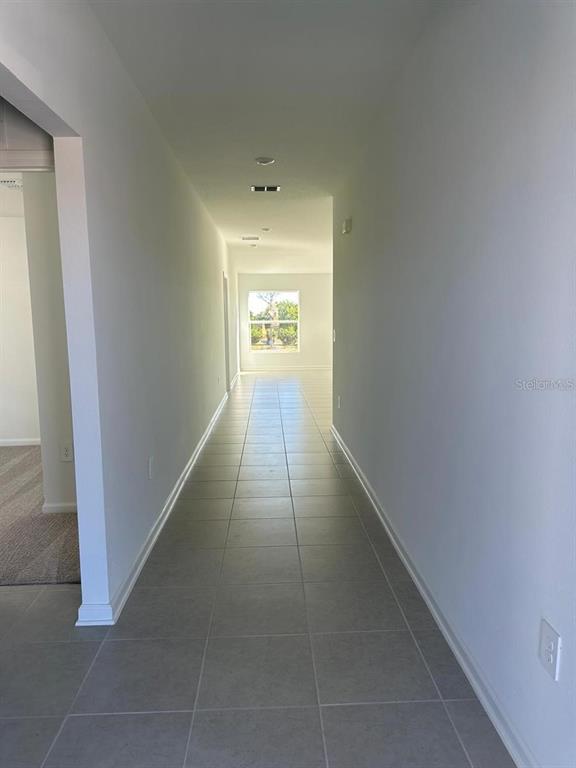 A long hallway with light gray tile flooring leads toward a window at the end — 2822 PENNACHIO DRIVE, LAKE WALES, FL