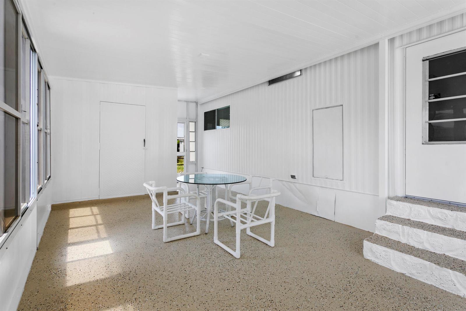 A white-walled enclosed porch features a glass-topped table, four chairs, and speckled flooring — 39016 Gayle Bay, Boynton Beach FL 33436, BOYNTON BEACH, FL