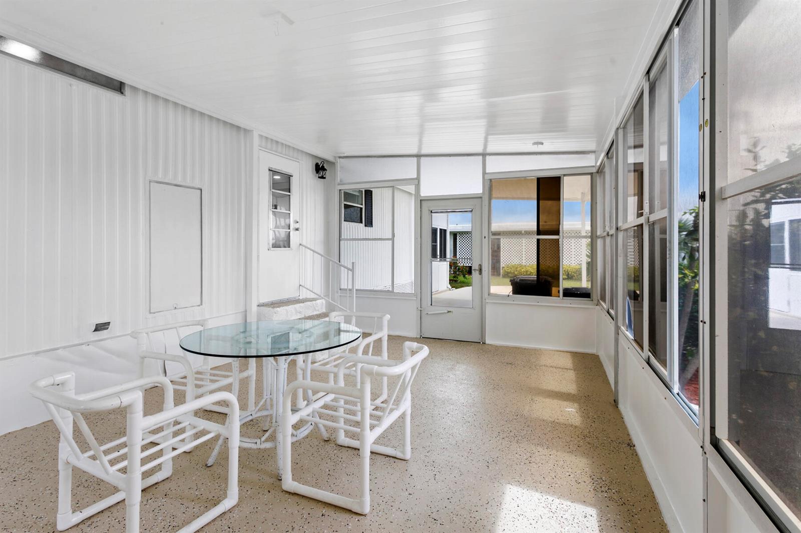 A screened-in porch features a glass-topped table, white chairs, and a speckled concrete floor — 39016 Gayle Bay, Boynton Beach FL 33436, BOYNTON BEACH, FL