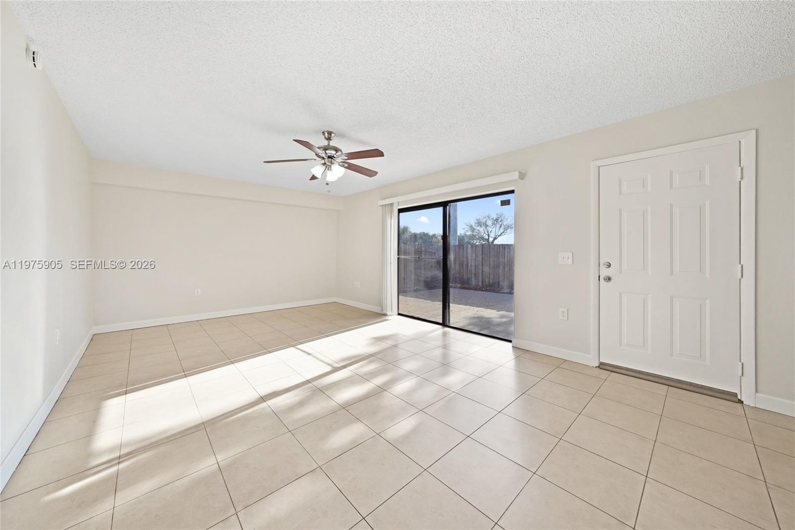 An empty room features beige tile flooring, a ceiling fan, and a sliding glass door — 2206 22nd Way, West Palm Beach FL 33407, WEST PALM BEACH, FL