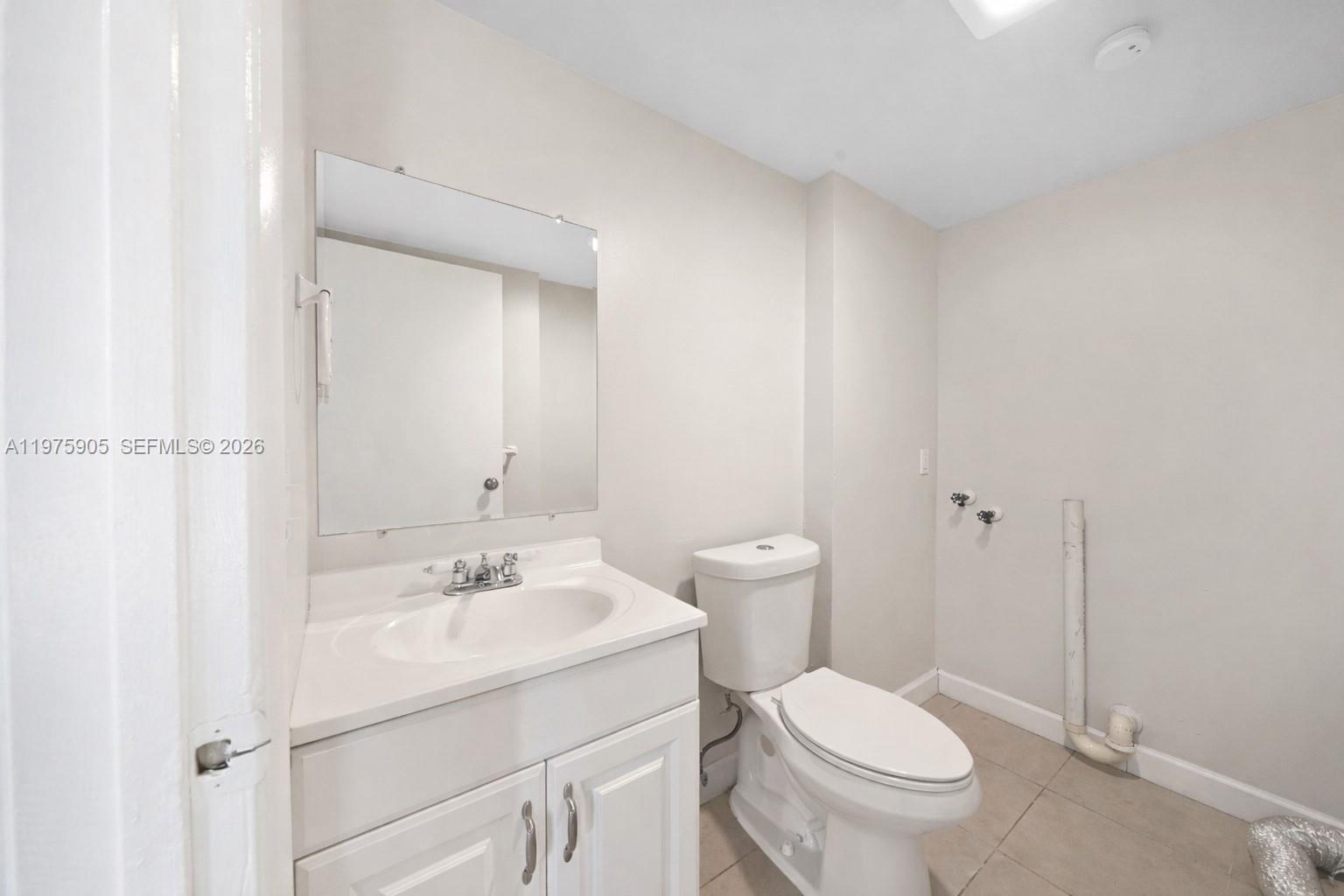A bathroom features a white vanity, a toilet, and exposed plumbing for a laundry machine — 2206 22nd Way, West Palm Beach FL 33407, WEST PALM BEACH, FL
