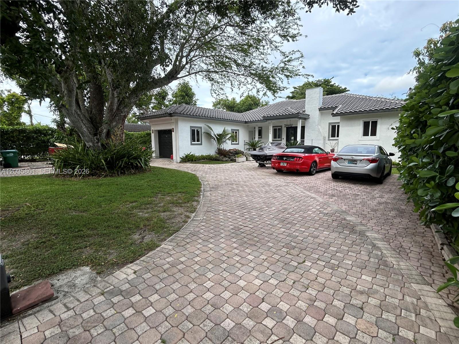 A white single-story house with a paved driveway, a large tree, and parked vehicles — 12885 SW 77 AVE, Pinecrest FL 33156, PINECREST, FL