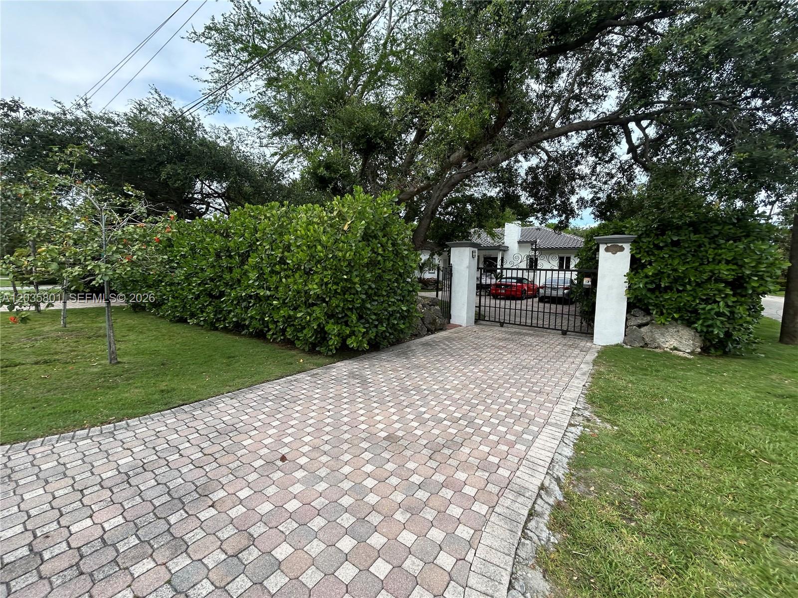 A paved driveway leads to a gated entrance with white pillars and a house beyond — 12885 SW 77 AVE, Pinecrest FL 33156, PINECREST, FL