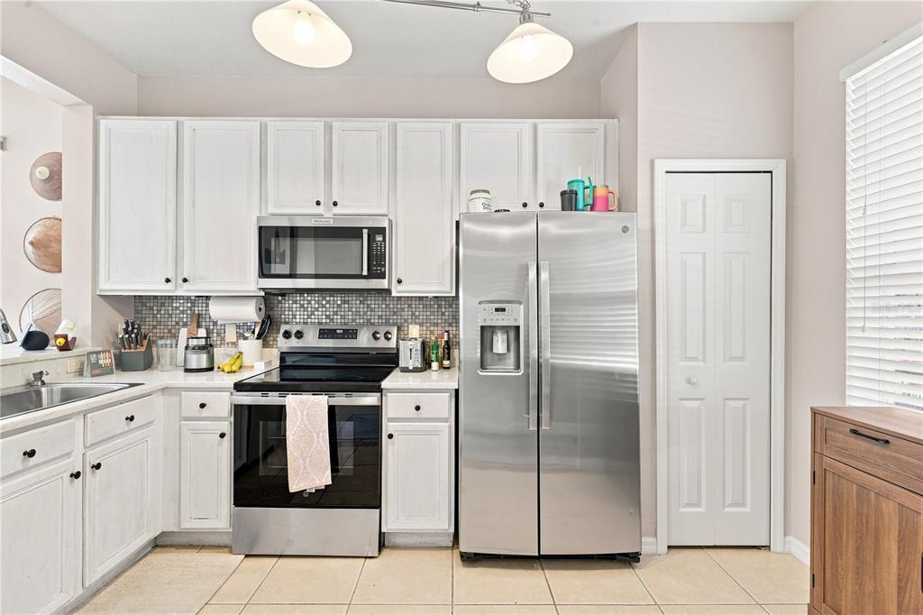 A kitchen features white cabinets, stainless steel appliances, a mosaic tile backsplash, and tile flooring — 1610 RETREAT VIEW CIRCLE, SANFORD, FL
