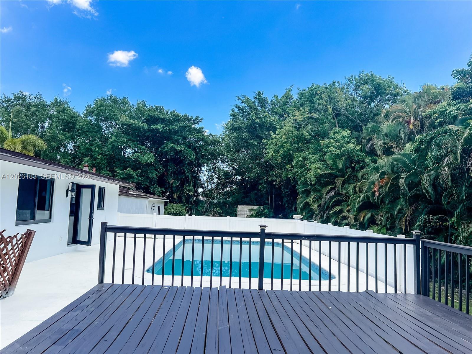 A wooden deck overlooks a swimming pool enclosed by a white fence and lush trees — 12200 NW 20th Ct, Plantation FL 33323, PLANTATION, FL