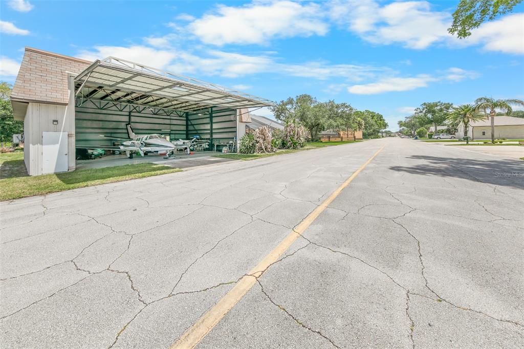 A small airplane is parked inside an open hangar next to a paved residential street — 38 LAZY EIGHT DRIVE, PORT ORANGE, FL