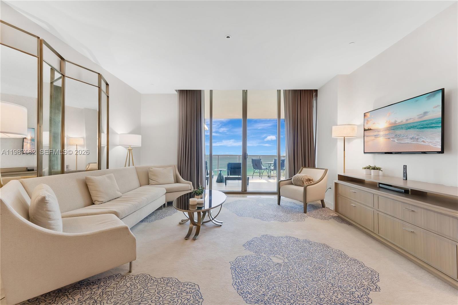 A living room features a beige sectional, a coffee table, and a balcony with ocean views — 9703 Collins Ave # 1006, Bal Harbour FL 33154, BAL HARBOUR, FL