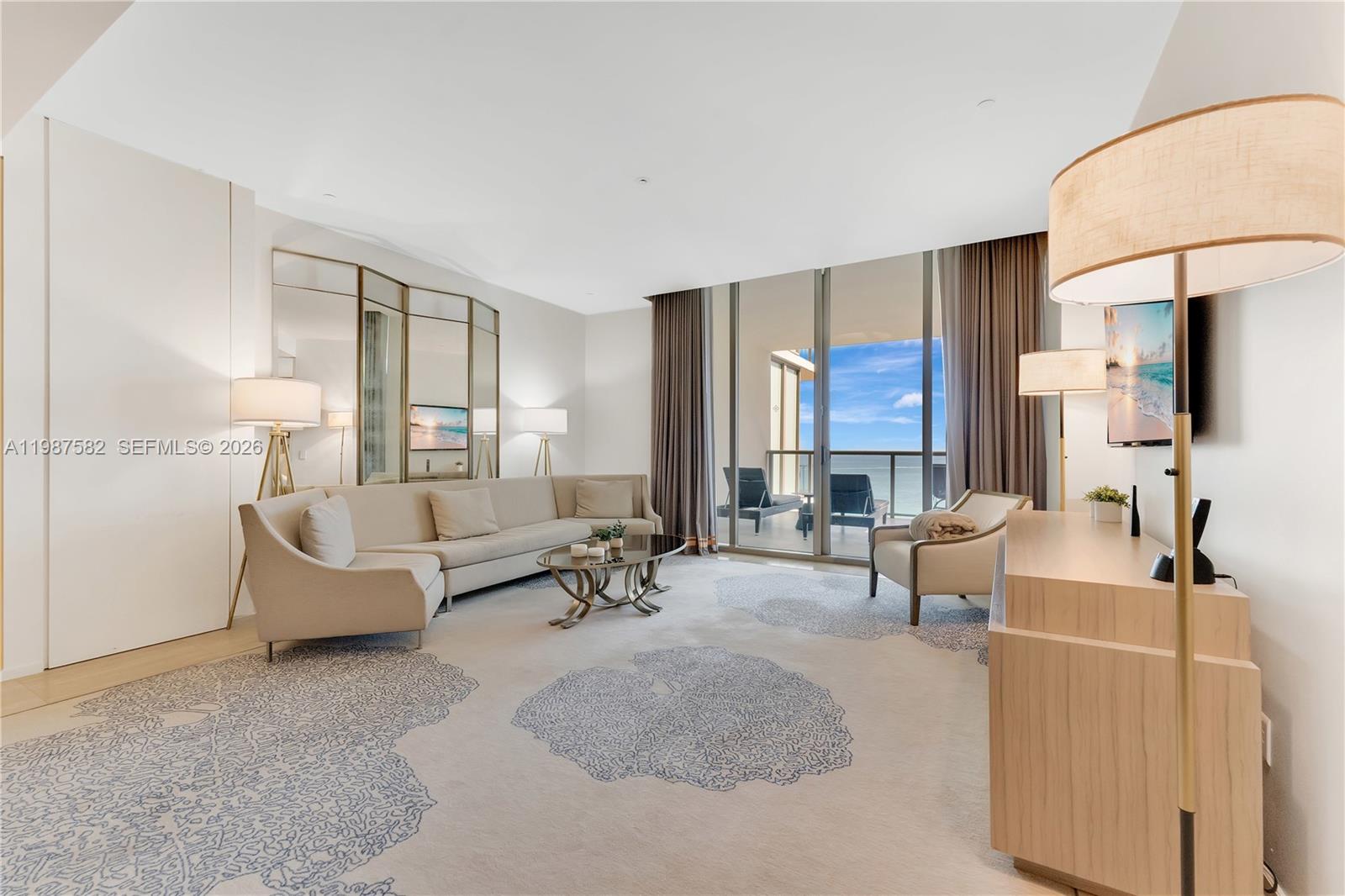 A bright living room features a beige sectional, patterned area rug, and floor-to-ceiling balcony doors — 9703 Collins Ave # 1006, Bal Harbour FL 33154, BAL HARBOUR, FL