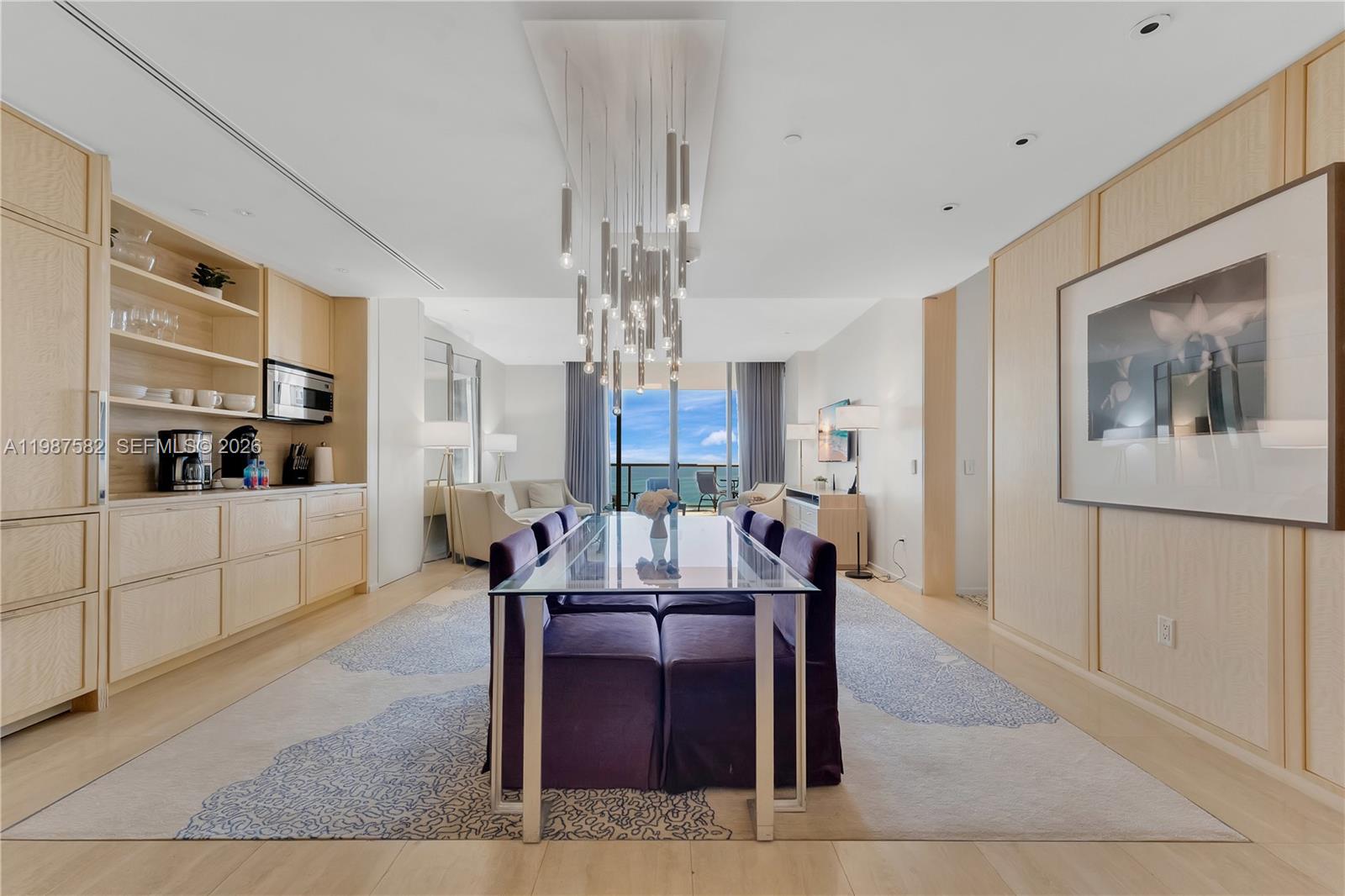 A dining room features a glass table, purple chairs, a modern chandelier, and light wood cabinetry — 9703 Collins Ave # 1006, Bal Harbour FL 33154, BAL HARBOUR, FL