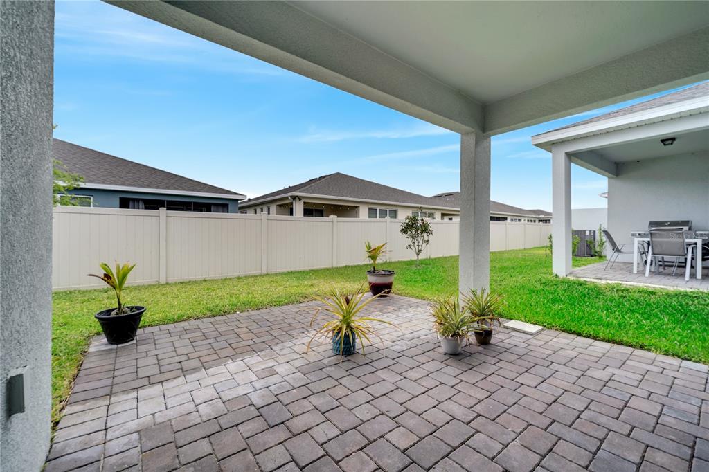 A paved patio with potted plants sits under a covered lanai in a fenced backyard — 1848 SPRING SHOWER CIRCLE, KISSIMMEE, FL