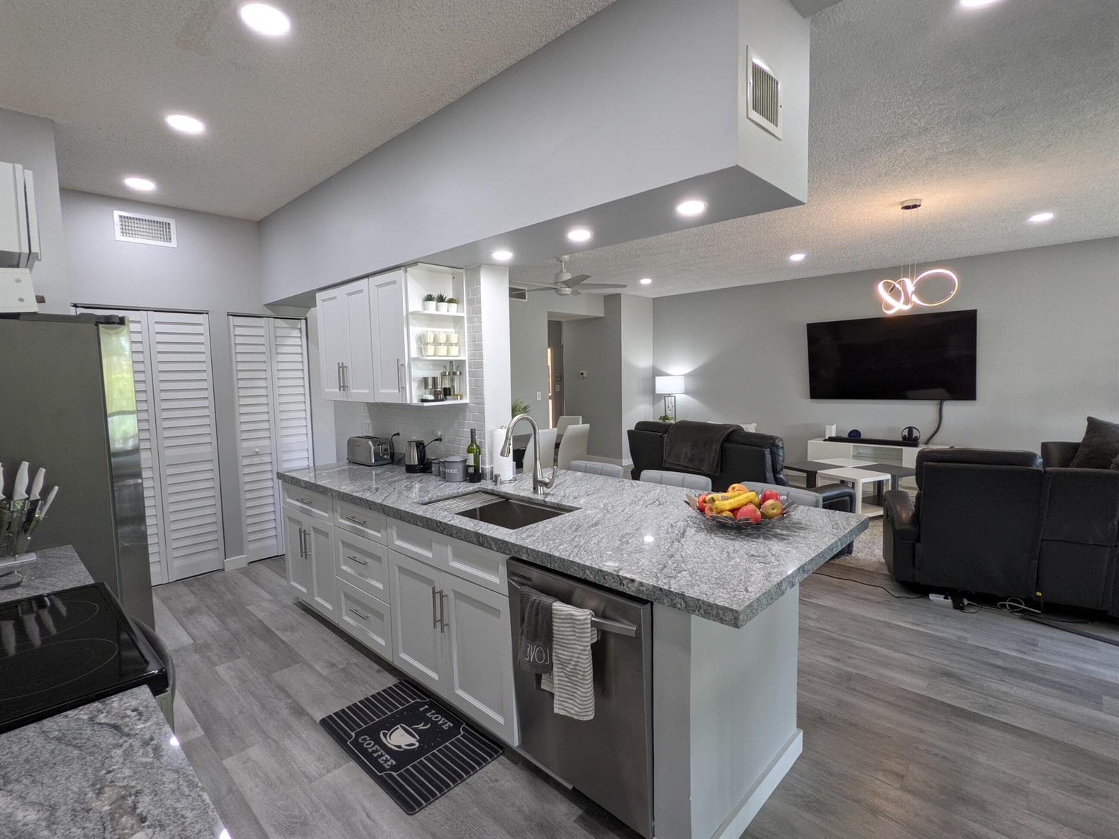 A kitchen with white cabinets and granite countertops opens into a living room area — 105 Half Moon Circle # F2, Hypoluxo FL 33462, HYPOLUXO, FL