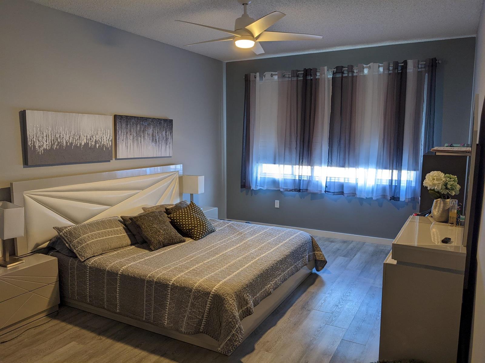 A bedroom features a white geometric headboard, grey bedding, wood-look flooring, and a ceiling fan — 105 Half Moon Circle # F2, Hypoluxo FL 33462, HYPOLUXO, FL