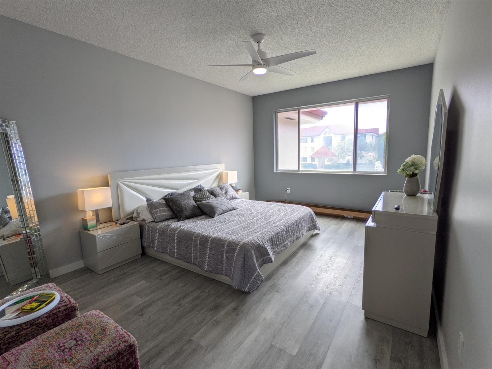 A bedroom features gray walls, wood-look flooring, a white headboard, and a large window — 105 Half Moon Circle # F2, Hypoluxo FL 33462, HYPOLUXO, FL