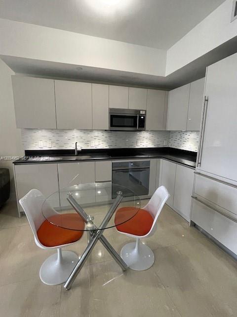 A modern kitchen features white flat-panel cabinetry, stainless steel appliances, and a glass dining table — 1010 Brickell Ave # 3810, Miami FL 33131, MIAMI, FL