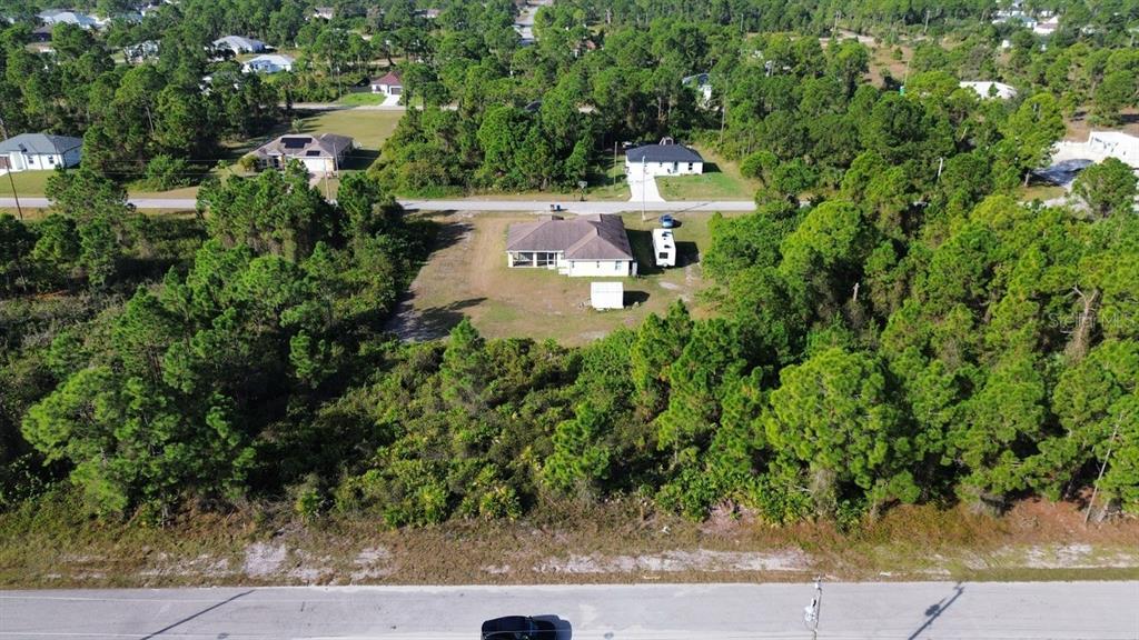 An aerial view shows a single-story house with a screened porch surrounded by wooded land — 710 RANDALL AVENUE E, LEHIGH ACRES, FL