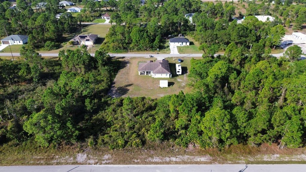 An aerial view shows a single-story house surrounded by dense trees and a paved road — 710 RANDALL AVENUE E, LEHIGH ACRES, FL