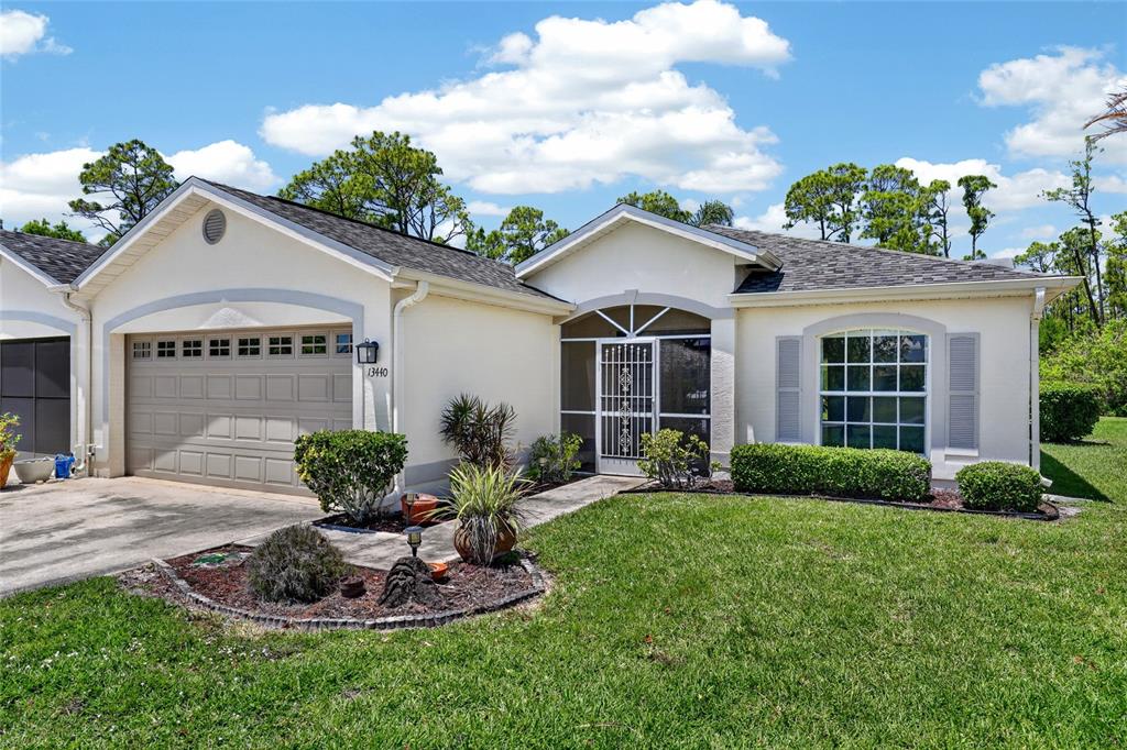 A single-story house with a beige stucco exterior, a two-car garage, and a screened entryway — 13440 SW PEMBROKE CIRCLE N, LAKE SUZY, FL