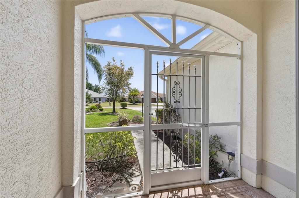 A view from a covered porch through a screened door toward a suburban neighborhood — 13440 SW PEMBROKE CIRCLE N, LAKE SUZY, FL