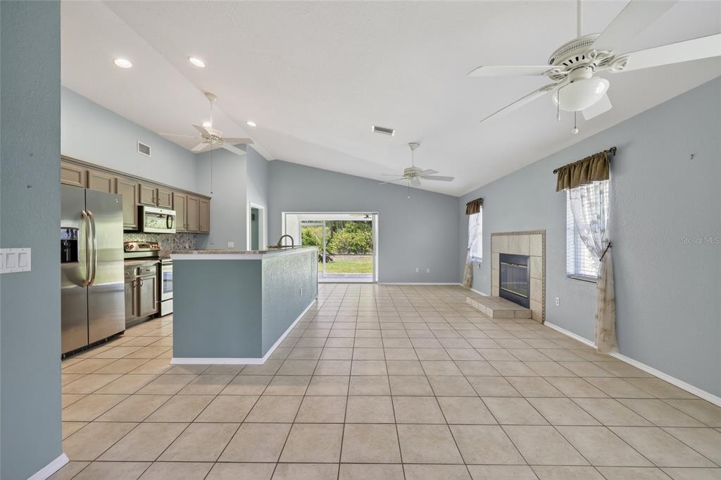 An open-concept living area features a kitchen with stainless appliances, tile flooring, and a fireplace — 13440 SW PEMBROKE CIRCLE N, LAKE SUZY, FL