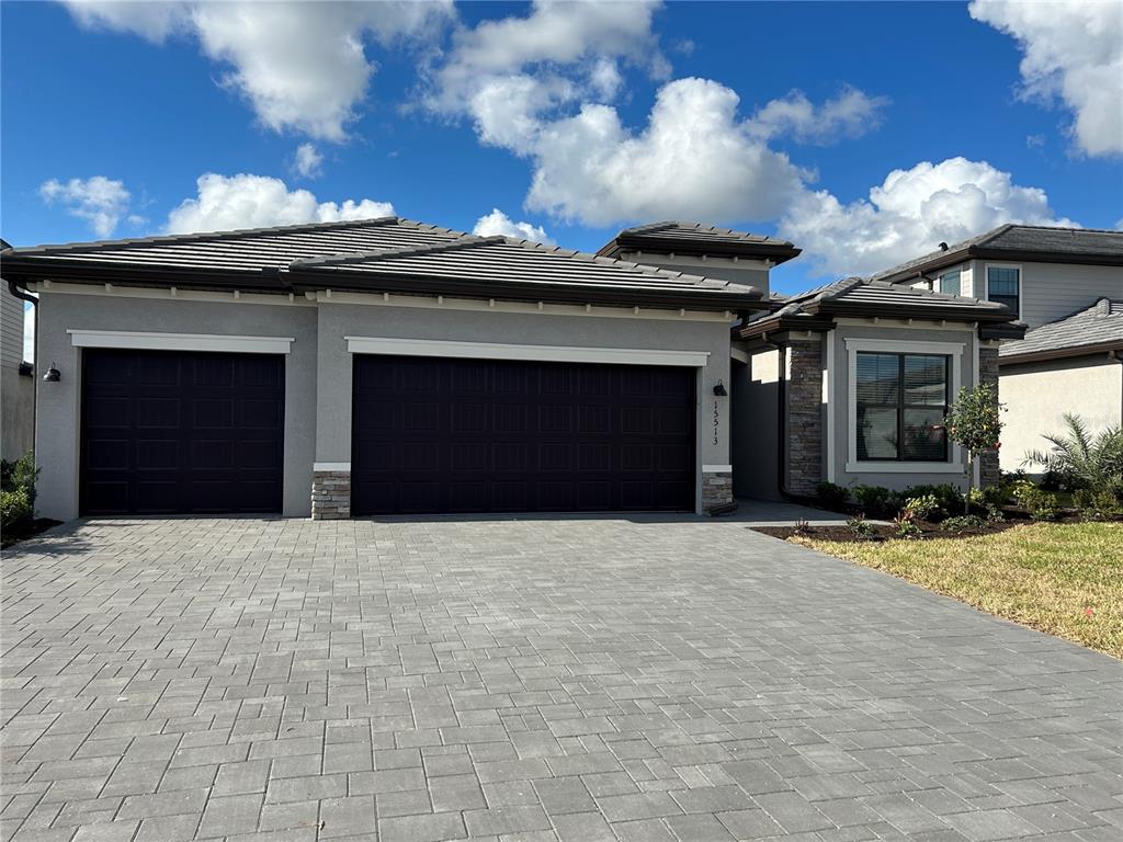 A gray house exterior features a three-car garage, stone accents, and a paved driveway — 15513 WHITE LINEN DRIVE, LAKEWOOD RANCH, FL