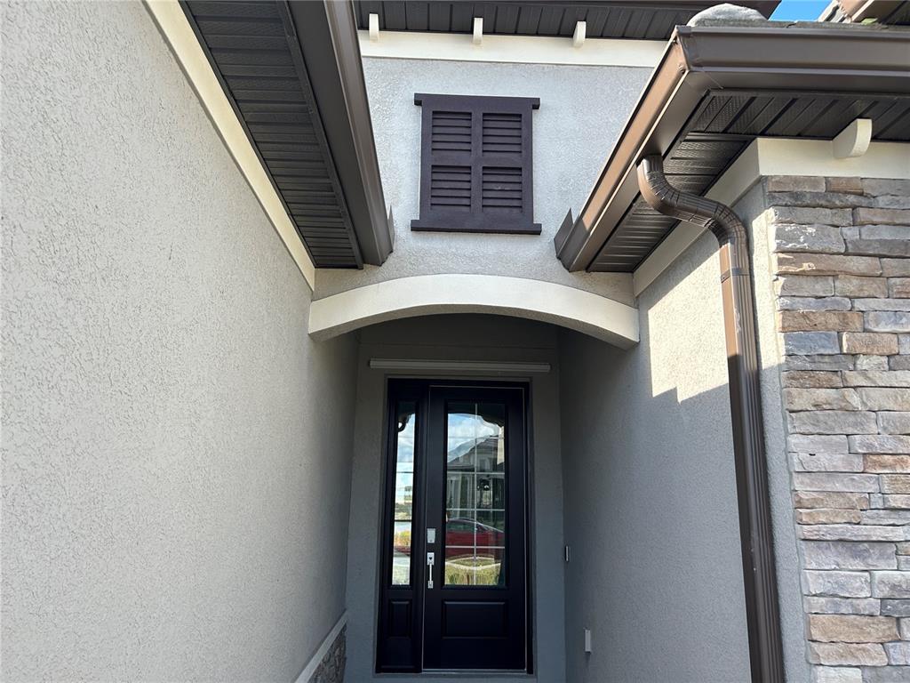 A front entryway features a dark glass-paneled door, a decorative shutter, and stone siding — 15513 WHITE LINEN DRIVE, LAKEWOOD RANCH, FL