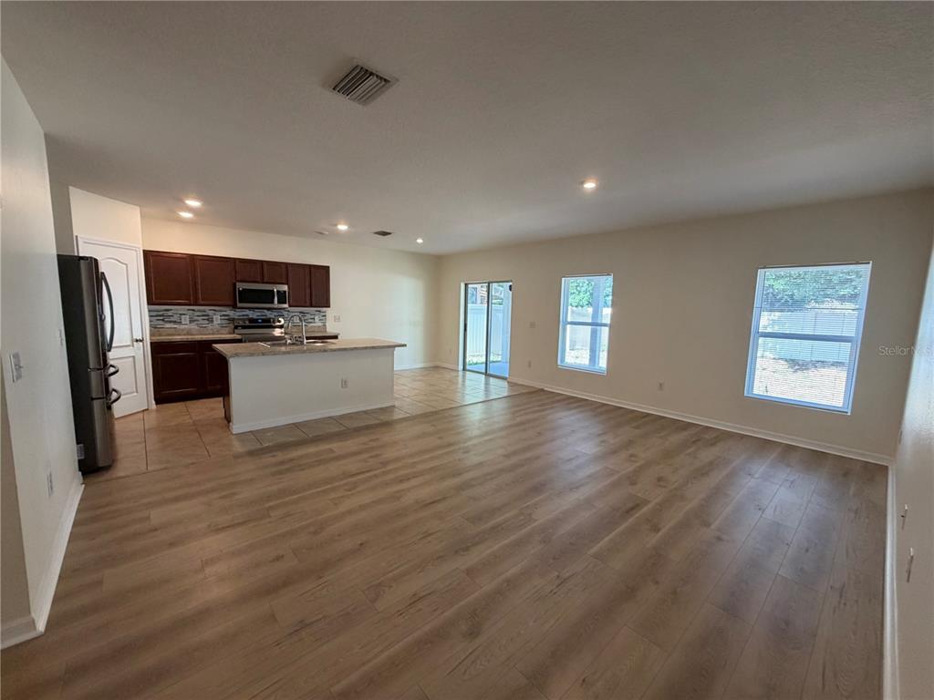 An open-concept kitchen and living area features wood-look flooring, dark cabinetry, and a center island — 10119 CANDLEBERRY WOODS LANE, GIBSONTON, FL