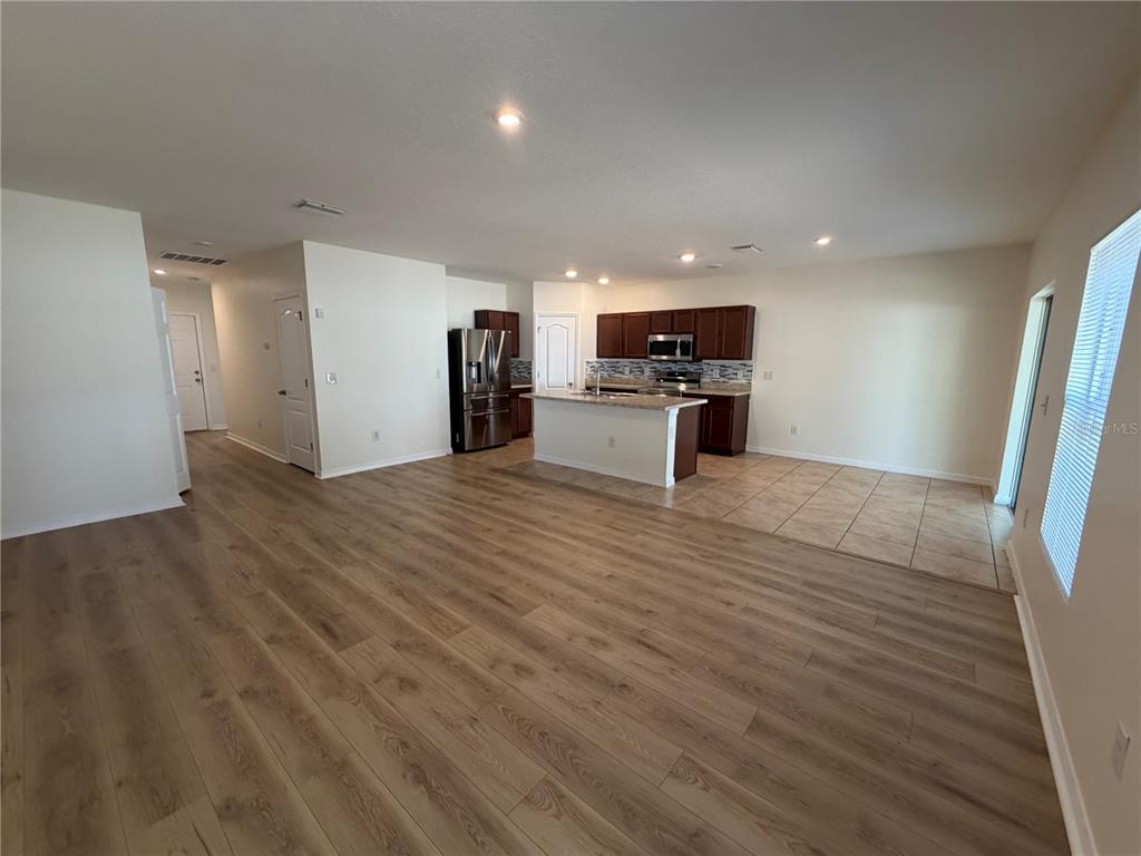 An open-concept kitchen and living area feature wood-look flooring, a center island, and dark cabinetry — 10119 CANDLEBERRY WOODS LANE, GIBSONTON, FL