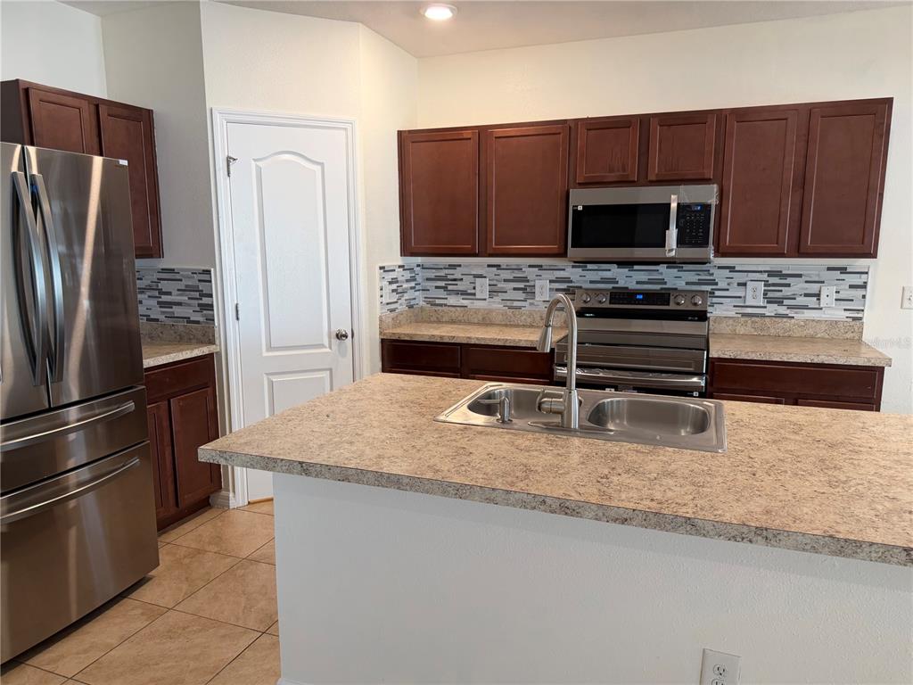 A kitchen features dark wood cabinets, stainless steel appliances, a center island, and tiled backsplash — 10119 CANDLEBERRY WOODS LANE, GIBSONTON, FL