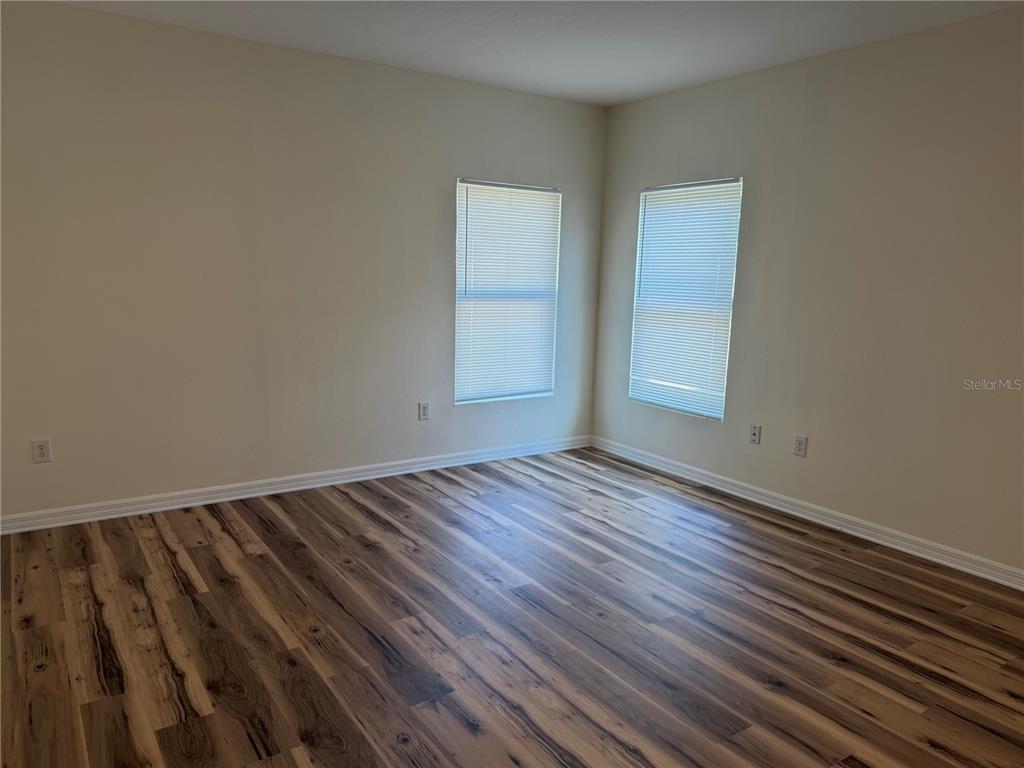An empty room features light-colored walls, two windows with blinds, and wood-look flooring — 10119 CANDLEBERRY WOODS LANE, GIBSONTON, FL