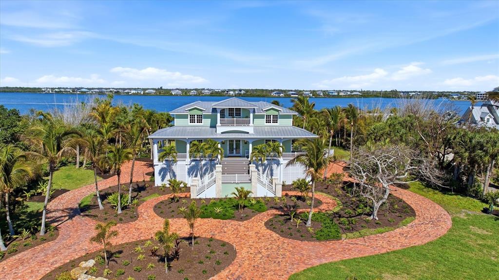 An elevated light green house with a metal roof sits behind a curved brick driveway — 10460 SUNNY DREAMS TERRACE, PLACIDA, FL