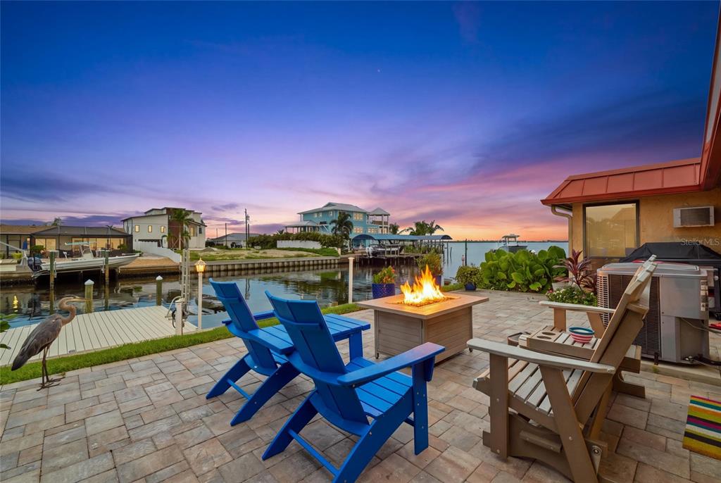 A patio with a fire pit and blue chairs overlooks a canal at sunset — 3844 CATALINA DRIVE UNIT 3844, BRADENTON, FL