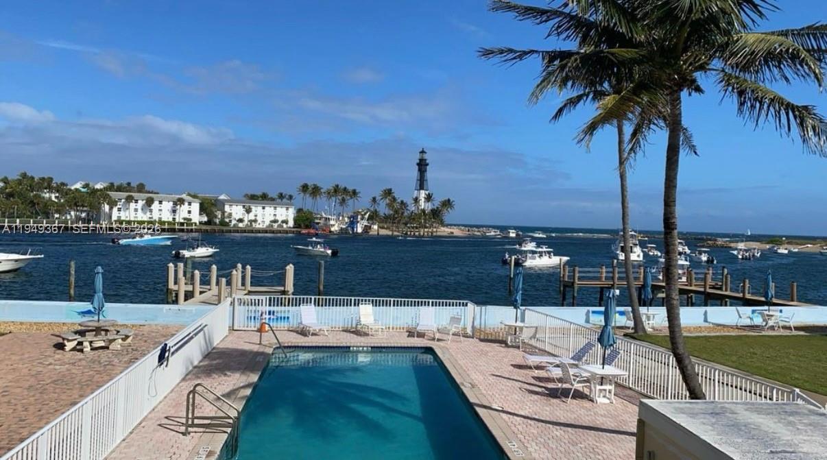 A swimming pool overlooks a waterway with boats and a distant lighthouse under a blue sky — 2508 Bay Dr # 12, Pompano Beach FL 33062, POMPANO BEACH, FL