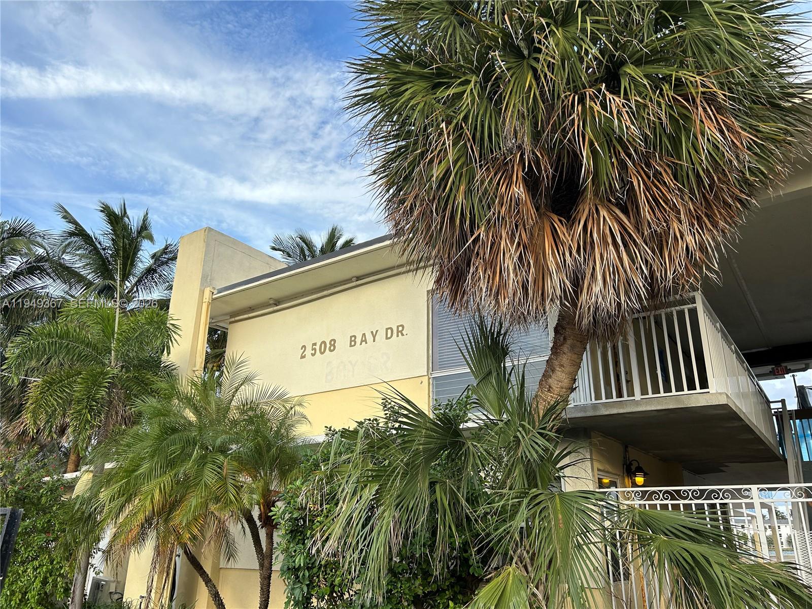 A low-angle view shows the exterior of a building with palm trees and a balcony — 2508 Bay Dr # 12, Pompano Beach FL 33062, POMPANO BEACH, FL