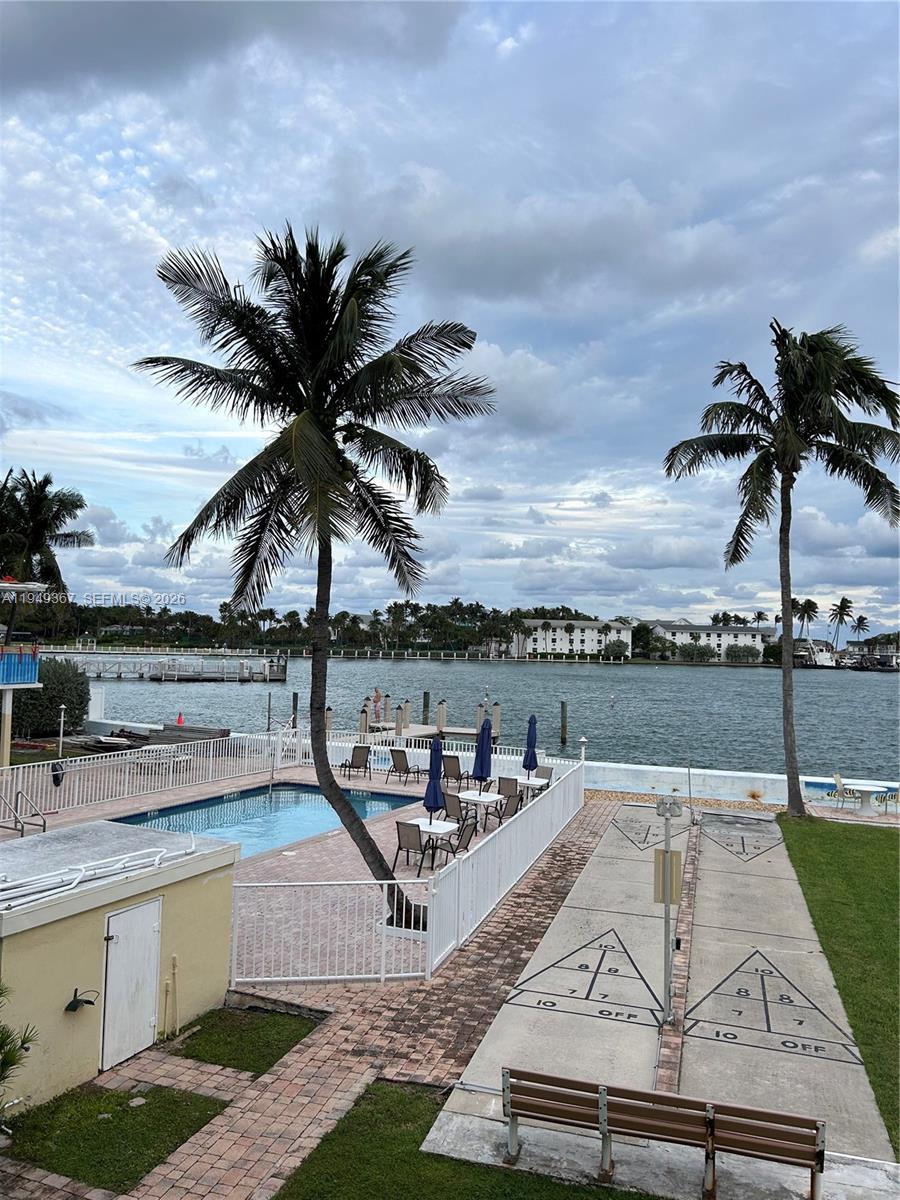 An outdoor pool area features shuffleboard courts, palm trees, and a view of the water — 2508 Bay Dr # 12, Pompano Beach FL 33062, POMPANO BEACH, FL