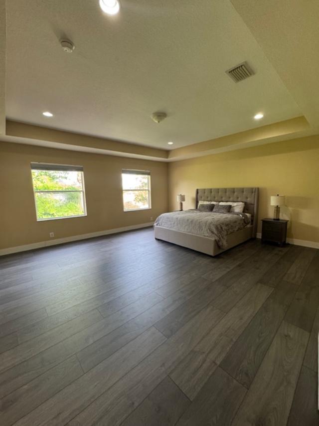 A spacious bedroom features a tray ceiling, two windows, and dark wood-look flooring — 1033 Grove Park Circle, Boynton Beach FL 33436, BOYNTON BEACH, FL