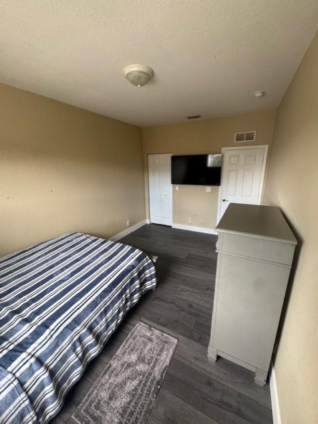 A bedroom features a bed with a striped blanket, a dresser, and a wall-mounted television — 1033 Grove Park Circle, Boynton Beach FL 33436, BOYNTON BEACH, FL