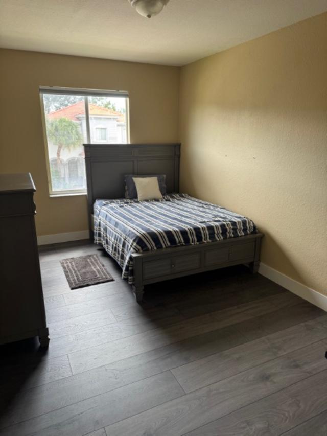 A bedroom with a gray bed frame, striped bedding, and dark wood-look flooring — 1033 Grove Park Circle, Boynton Beach FL 33436, BOYNTON BEACH, FL