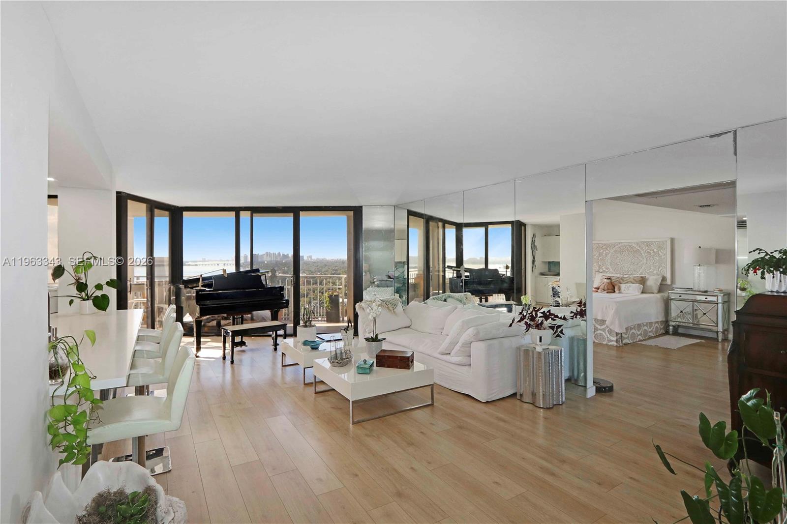 A living room with light wood floors, a white sofa, a piano, and mirrored walls — 1000 Quayside Ter # 1608, Miami FL 33138, MIAMI, FL