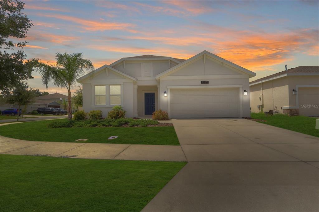 A single-story suburban house with a two-car garage and a palm tree at sunset — 33571 SKY BLOSSOM CIRCLE, LEESBURG, FL