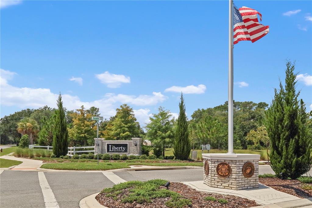 A brick monument sign for Liberty Preserve stands near a flagpole with an American flag — 33571 SKY BLOSSOM CIRCLE, LEESBURG, FL