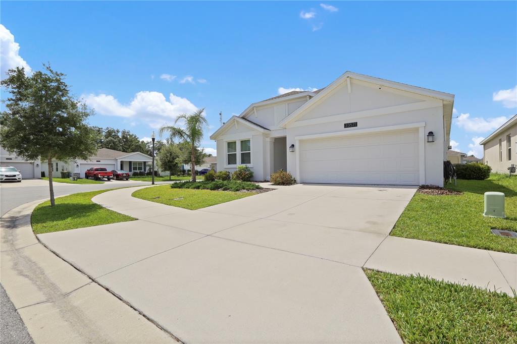 A single-story house with a white exterior, a two-car garage, and a concrete driveway — 33571 SKY BLOSSOM CIRCLE, LEESBURG, FL