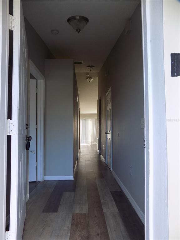 A hallway with wood-look flooring leads toward a bright room with vertical blinds — 628 BLUEBILL COURT, POINCIANA, FL