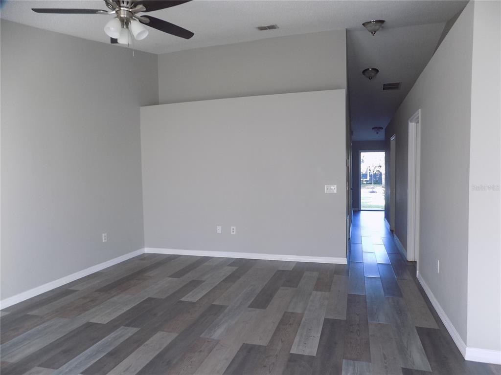 An empty living room features gray walls, wood-look flooring, a ceiling fan, and a hallway — 628 BLUEBILL COURT, POINCIANA, FL