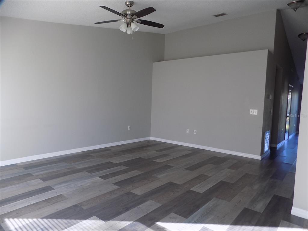 An empty room features gray walls, a ceiling fan, and wood-look plank flooring — 628 BLUEBILL COURT, POINCIANA, FL