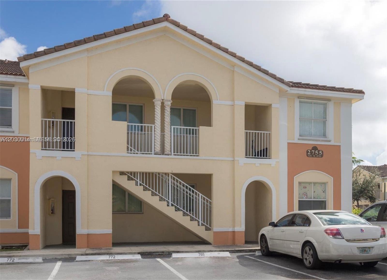 A two-story stucco apartment building features arched balconies, a central staircase, and assigned parking spaces — 2755 SE 16th Ave # 202, Homestead FL 33035, HOMESTEAD, FL