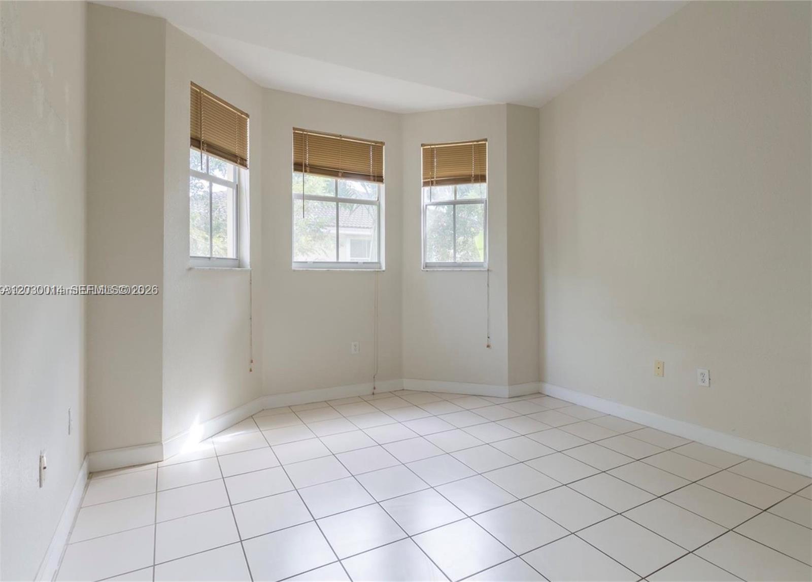 An empty room features white tile flooring, beige walls, and a three-window bay area — 2755 SE 16th Ave # 202, Homestead FL 33035, HOMESTEAD, FL