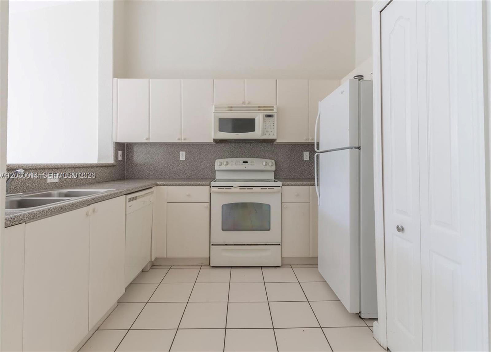 A kitchen features white cabinets, white appliances, speckled countertops, and light-colored floor tiles — 2755 SE 16th Ave # 202, Homestead FL 33035, HOMESTEAD, FL
